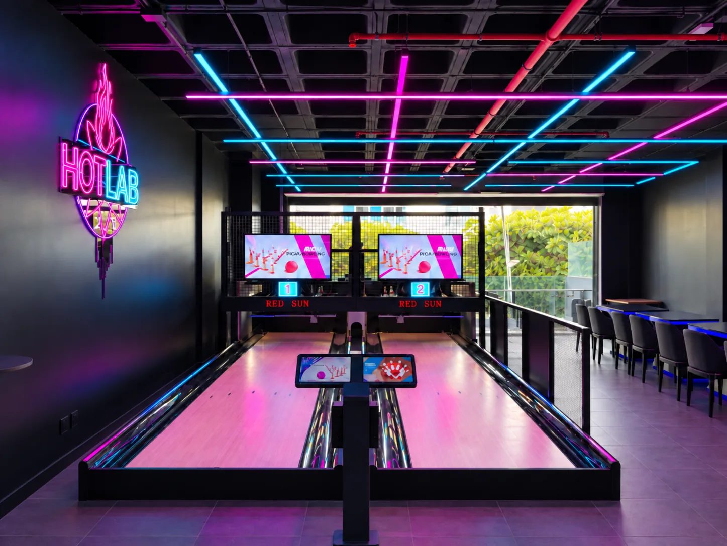 Las dos pistas reales de mini bolos de HOTLAB Lanzarote bajo las luces de neón, con el cartel HOTLAB y las mesas del local